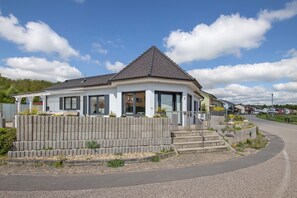 Une maison moderne avec un toit en pente, un mur de soutènement en pierre et une allée pavée.