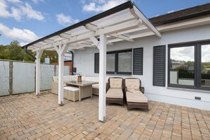 Un patio couvert aménagé avec des meubles en osier, une table et des chaises.