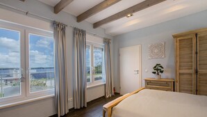 A bedroom with a bed, a window with curtains, a door, a bedside table with a plant, and a wardrobe. - Holiday Home Seepanorama - Marina Mücheln with Lake View, Private Terrace & Wi-Fi (Mücheln (Geiseltal))