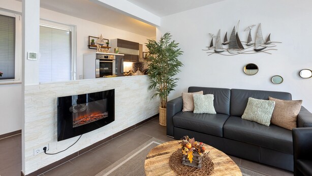 Un salon moderne avec une cheminée, un canapé en cuir noir, une table basse ronde et un téléviseur fixé au mur.