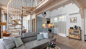 A modern living room with a grey sofa, a wooden spiral staircase, and a kitchen area in the background. - Holiday Apartment 'Seeschwalbe - Marina Mücheln' with Lake View, Wi-Fi & Air Conditioning (Mücheln (Geiseltal))