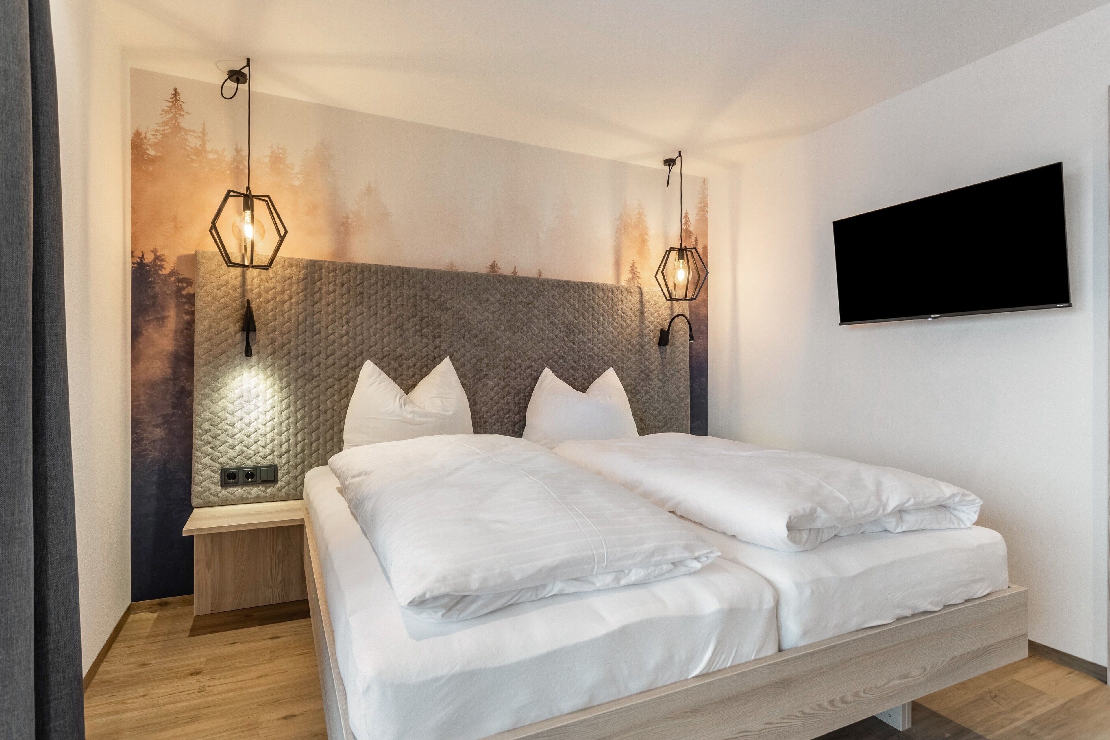 Un dormitorio moderno con cama, cabecera, televisor de pared y dos apliques.
