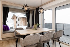 Un comedor moderno con una mesa de madera, sillas tapizadas en gris y vistas a un edificio de madera a través de amplios ventanales.