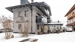 Ein modernes Gebäude mit geneigtem Dach, großen Fenstern und einer verschneiten Auffahrt.