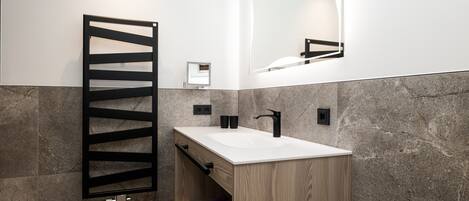 A modern bathroom with a wooden vanity, a black towel rack, a white sink, and a large mirror.