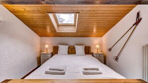 Un dormitorio con tragaluz, cabecera de madera, dos mesitas de noche con lámparas y toallas ordenadas.
