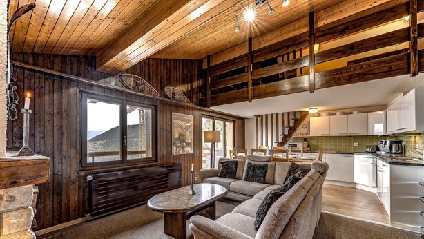 Un interior acogedor con techo de madera, un conjunto de sofás, una mesa de comedor y una zona de cocina.