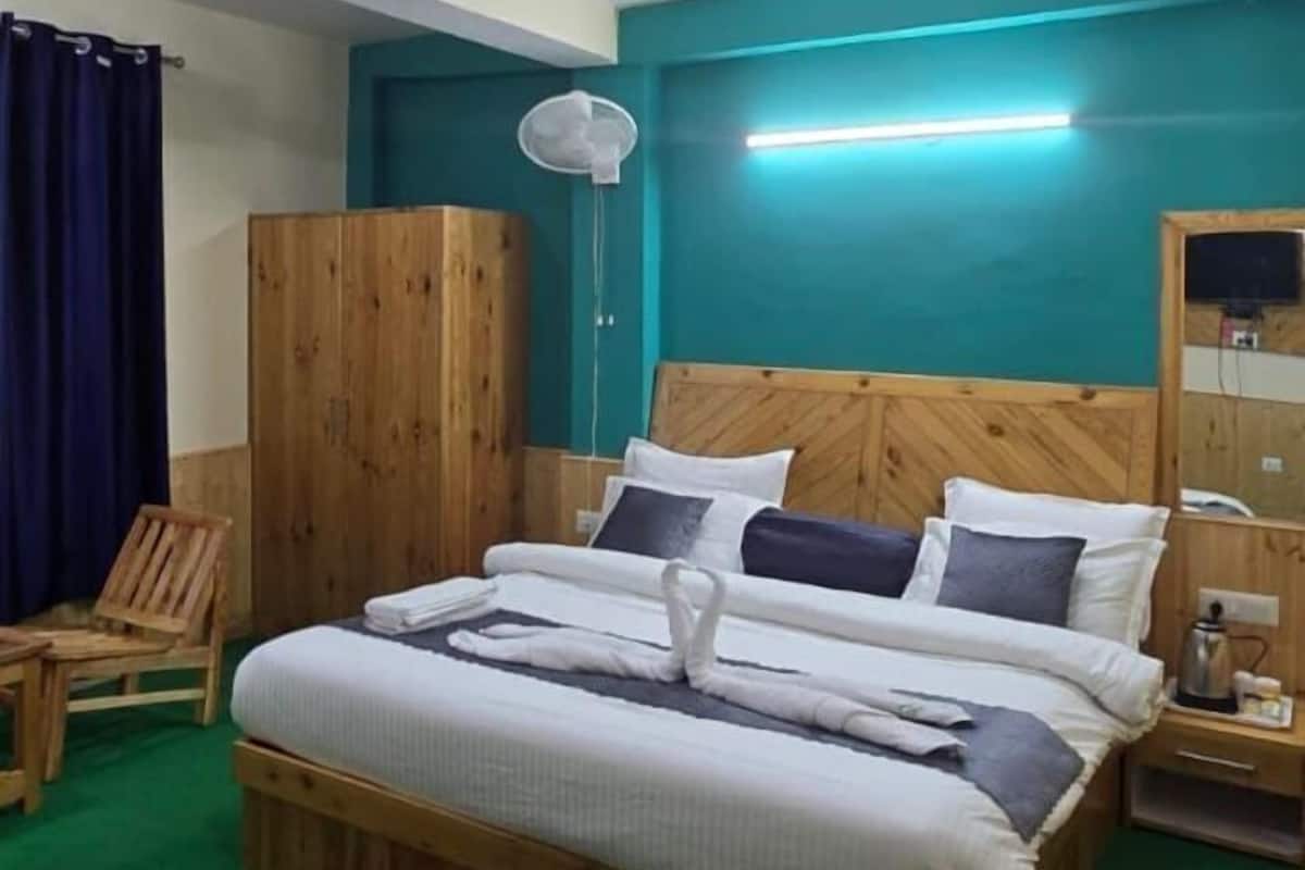 A bedroom with a wooden bed, a nightstand, a wooden wardrobe, a chair, and a green carpet.