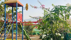 Un parque infantil con tobogán y estructuras para escalar, rodeado de follaje y un cielo despejado.