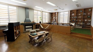 Una biblioteca con estanterías de madera, una zona de lectura con sillones y una chimenea.
