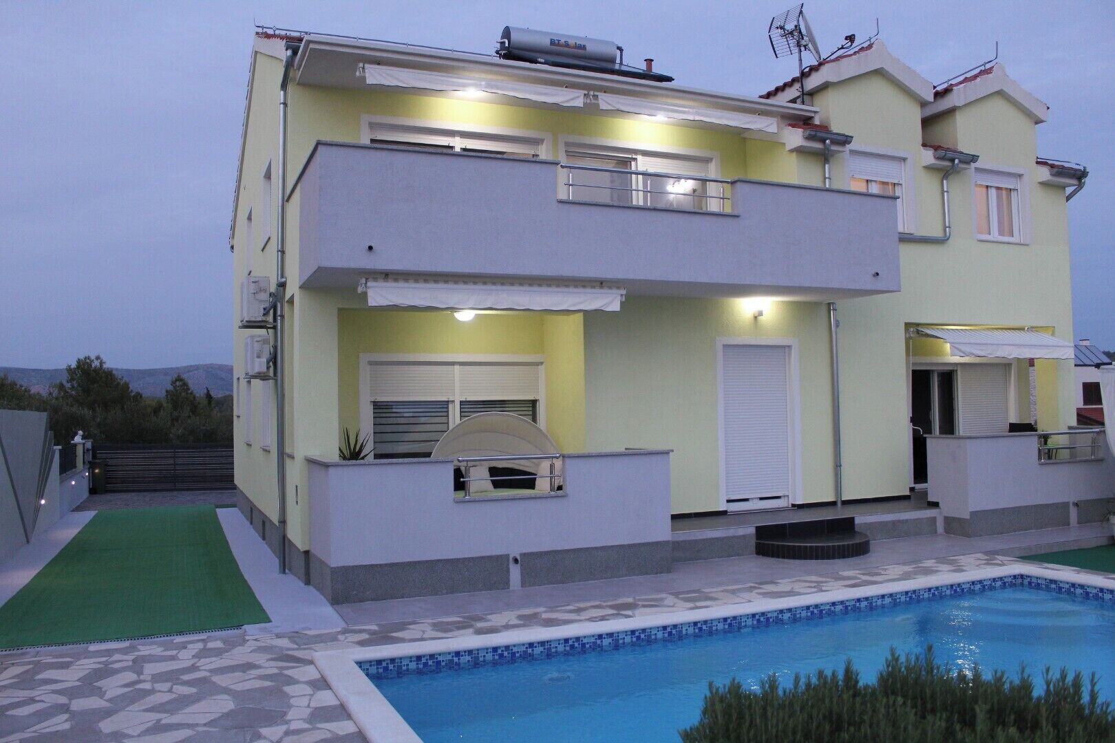 A two-story residential building with a swimming pool, a balcony, and a small outdoor grill area.