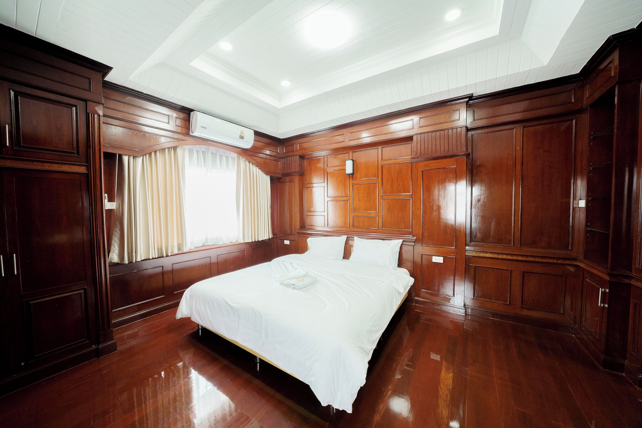 A spacious bedroom with a large bed, wooden paneling, and a ceiling light fixture.