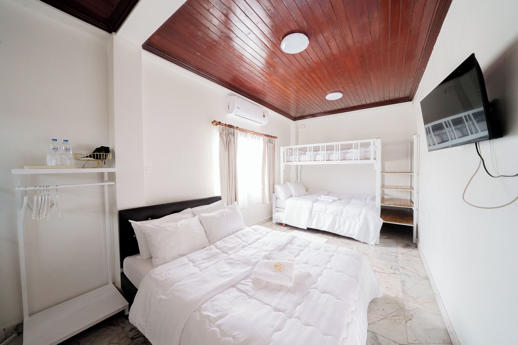 A hotel room with a wooden ceiling, a bed, a TV, a wardrobe, and a window with curtains.