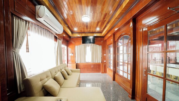 A room with a long beige sofa, wooden paneling, a large window with curtains, and a view of the outside. - The Star Pool Villa Hatyai (Hat Yai)