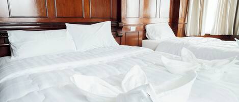 A hotel room with two beds, wooden paneling on the walls, and a window with curtains.