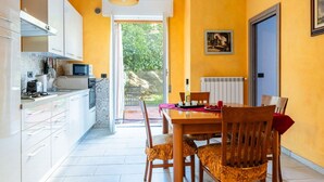 Cucina moderna con mobili bianchi, zona pranzo con tavolo e sedie in legno e vista su spazi verdi.
