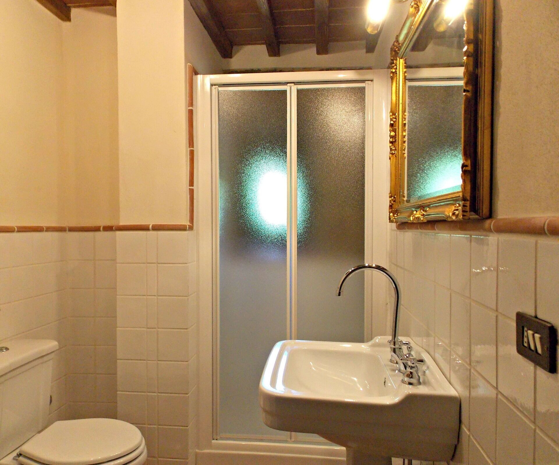 Baño con inodoro, lavabo y ducha con puertas de vidrio esmerilado.