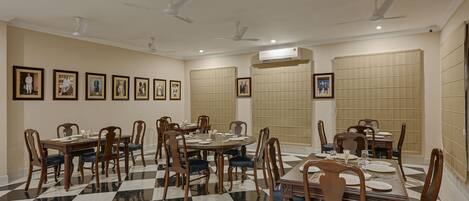 A dining area with multiple tables and chairs, ceiling fans, and framed pictures on the walls.