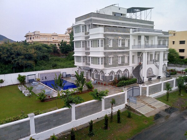 A multi-story building with a pool, surrounded by greenery and a white fence. - Boheda Manor (Udaipur)