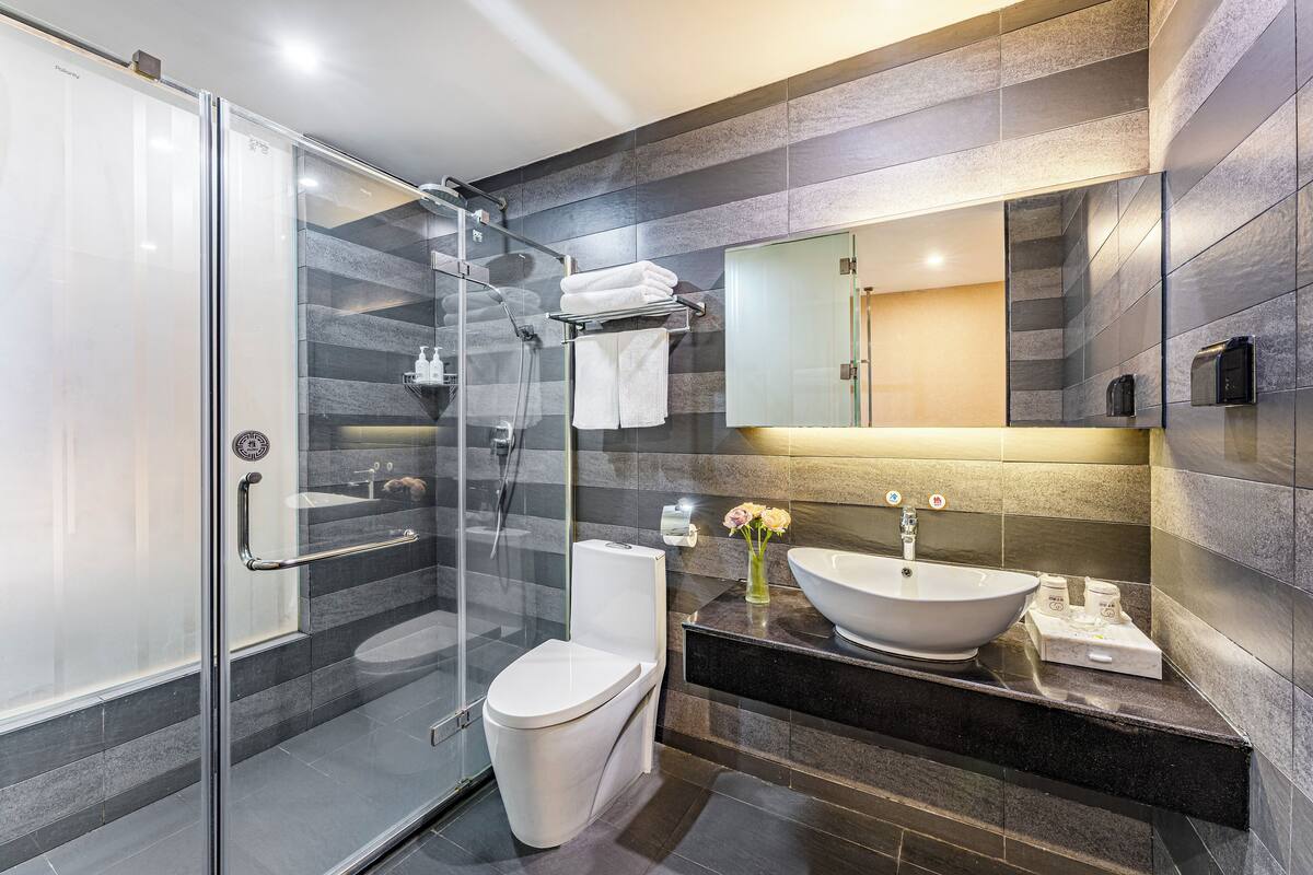 Un baño moderno con ducha envuelta en vidrio, inodoro blanco, un lavabo de diseño y encimera de mármol.