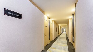 A hotel hallway with numbered doors, a carpeted floor, and a sign indicating room numbers.