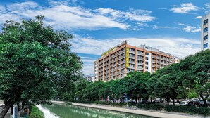 A multi-story hotel with a modern design, located beside a canal with lush greenery and trees.
