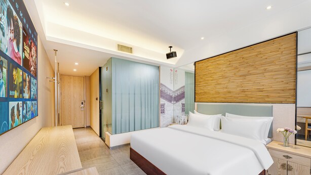 A modern hotel room with a large bed, a wooden headboard, a nightstand, and a wall-mounted TV.