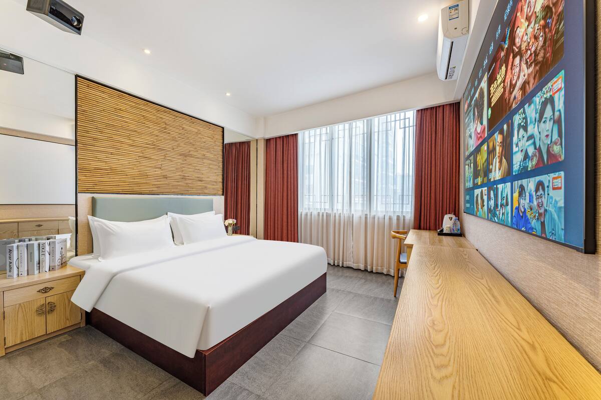 Una habitación de hotel moderna con una cama grande, cabecero de madera, un escritorio con una silla y una pared con un mural colorido.