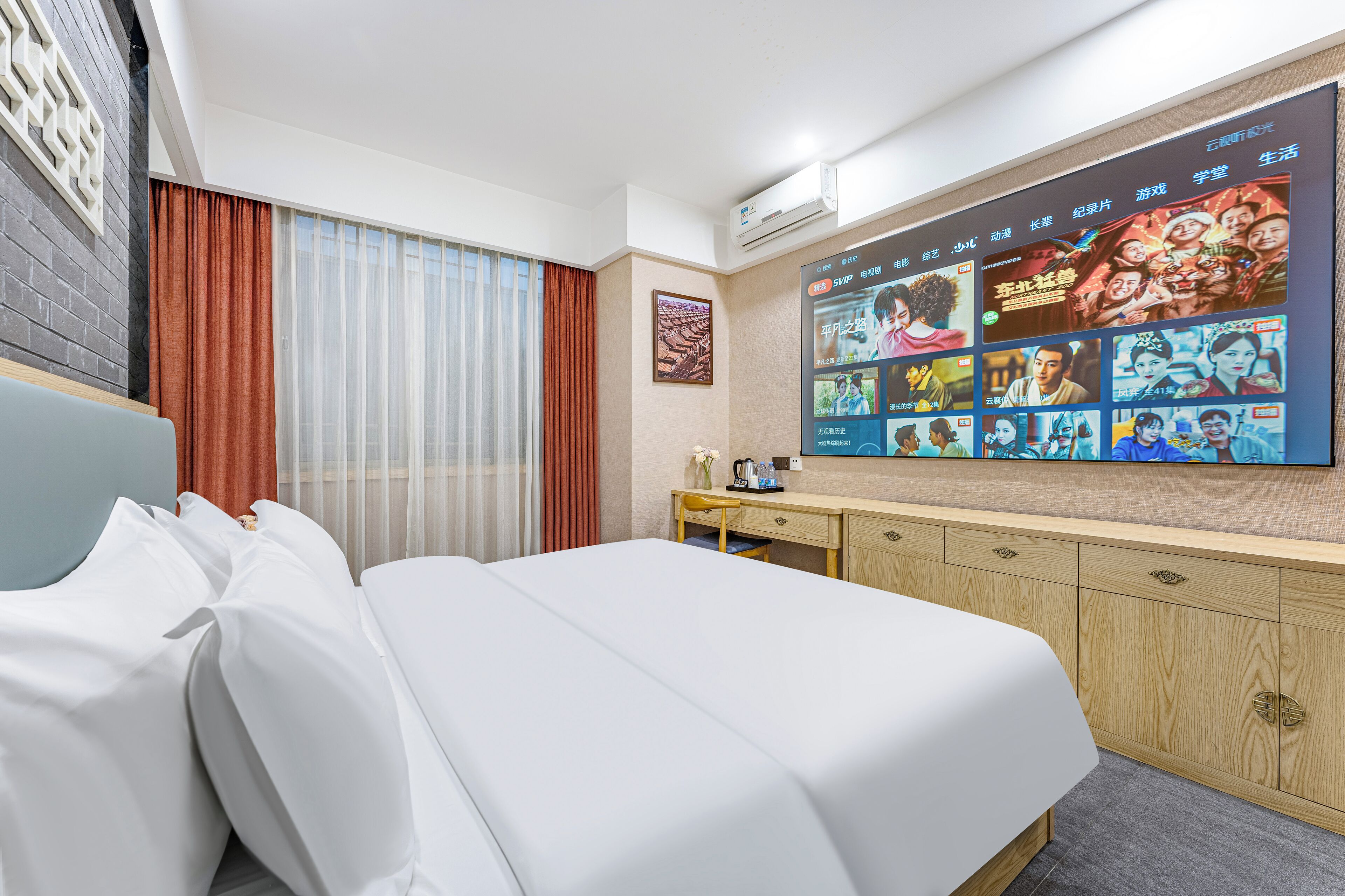 A hotel room with a large bed, a desk, a flat-screen TV mounted on the wall, and a window with curtains.