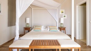 A four-poster canopy bed with a wooden bench in front, two bedside tables with lamps, and a neutral color scheme.