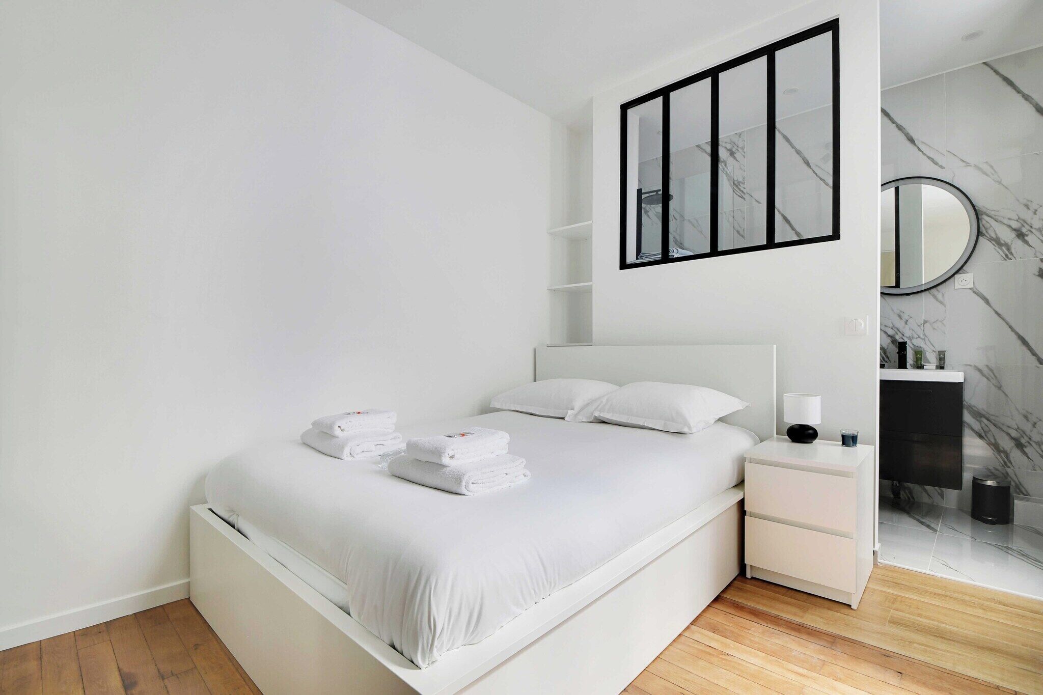 Een moderne slaapkamer met een groot bed, witte beddengoed, een nachtkastje, een spiegel en marmeren wanddecoraties.