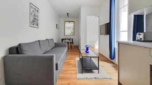Un salon moderne avec un canapé gris, une petite table basse et un coin cuisine équipé d’un four à micro-ondes.