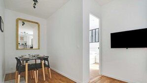 Un salon moderne comprenant un coin repas, un grand miroir et un téléviseur à écran plat fixé au mur.