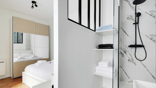 Een moderne hotelkamer met een groot bed, een inloopkast en een badkamer met douche en marmeren tegels.