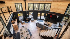 A spacious interior with a high ceiling, wooden walls, and large windows offering views of the surrounding forest.