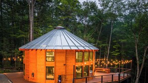 A wooden cabin with a metal roof, a deck, and string lights.