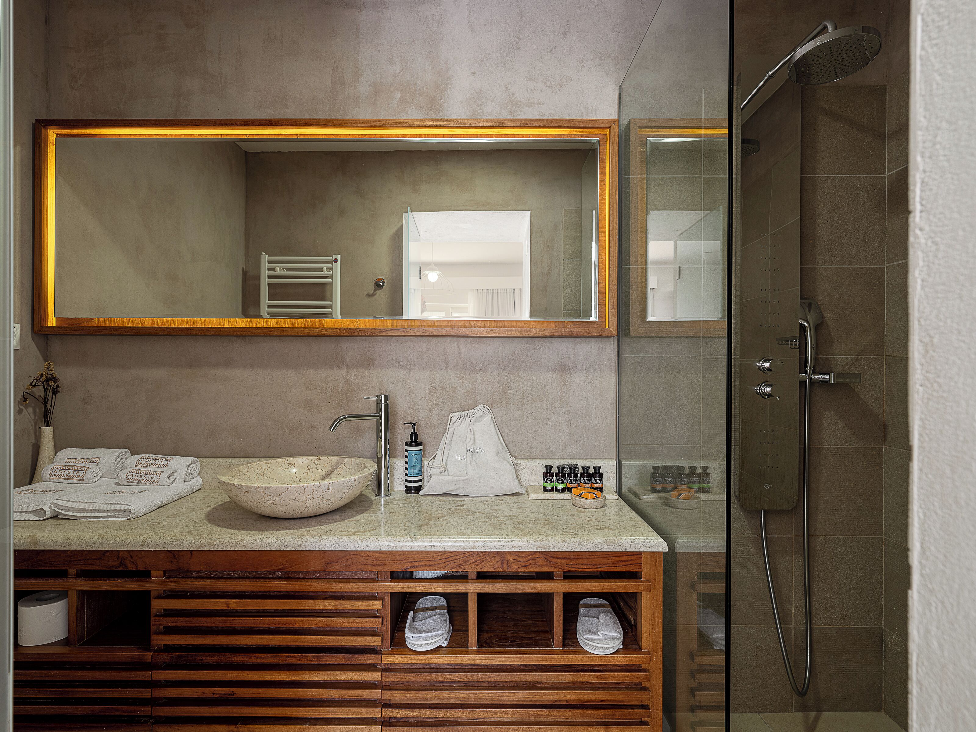 A bathroom with a large mirror, a sink, a shower, and a wooden vanity.