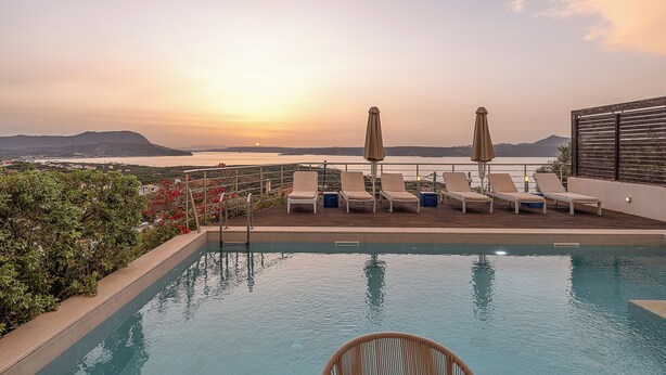 Ein Poolbereich mit Liegestühlen und Sonnenschirmen mit Blick auf ein Gewässer und die Ferne Hügel.