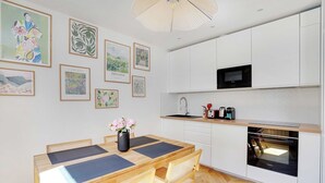 Una cocina moderna con armarios blancos, un microondas y un horno. Hay una mesa de comedor con sillas y un florero.