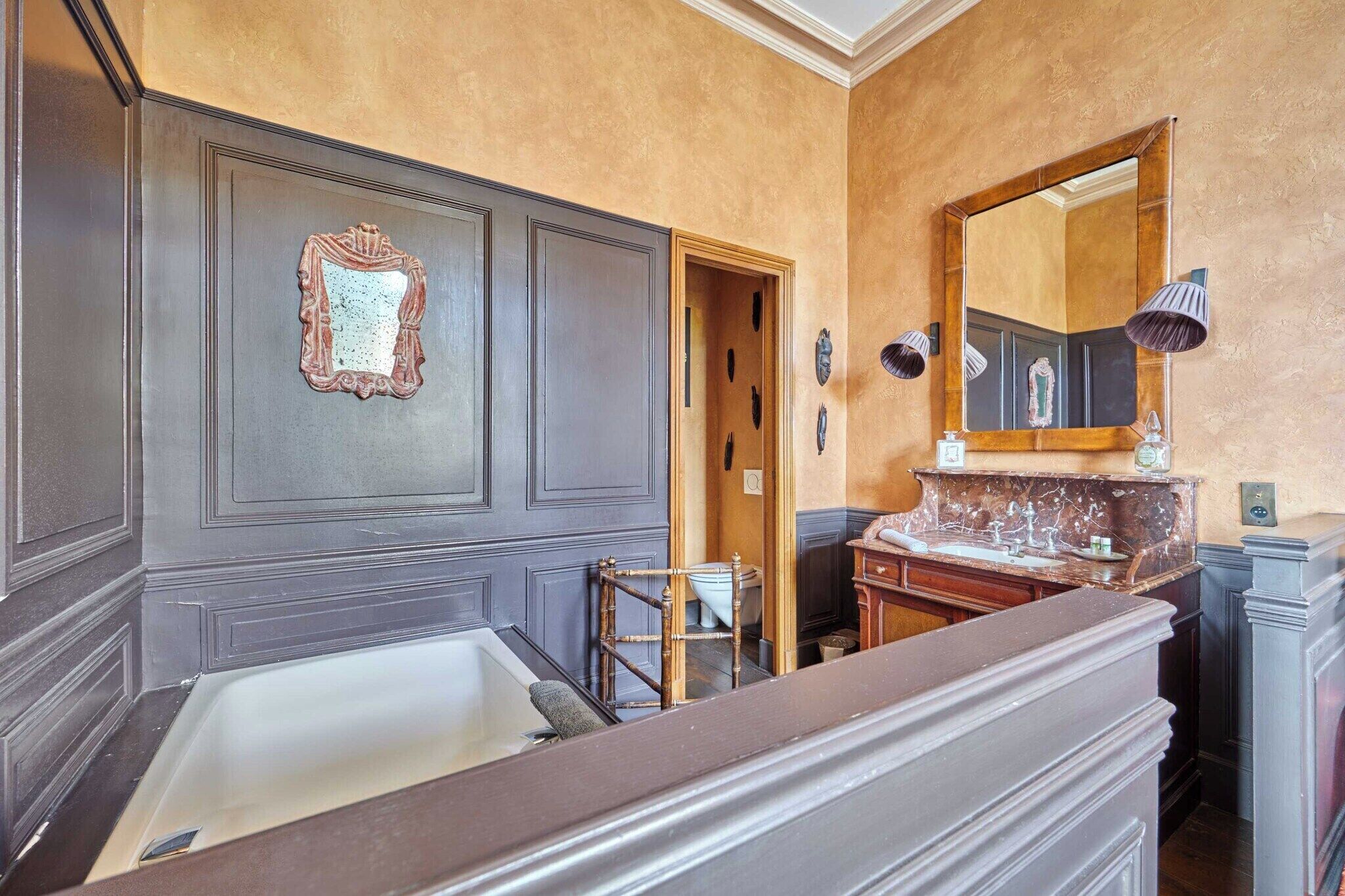 Une salle de bain dotée d’une grande baignoire, d’un meuble-lavabo avec un plan de travail en marbre et d’un miroir au-dessus du lavabo.