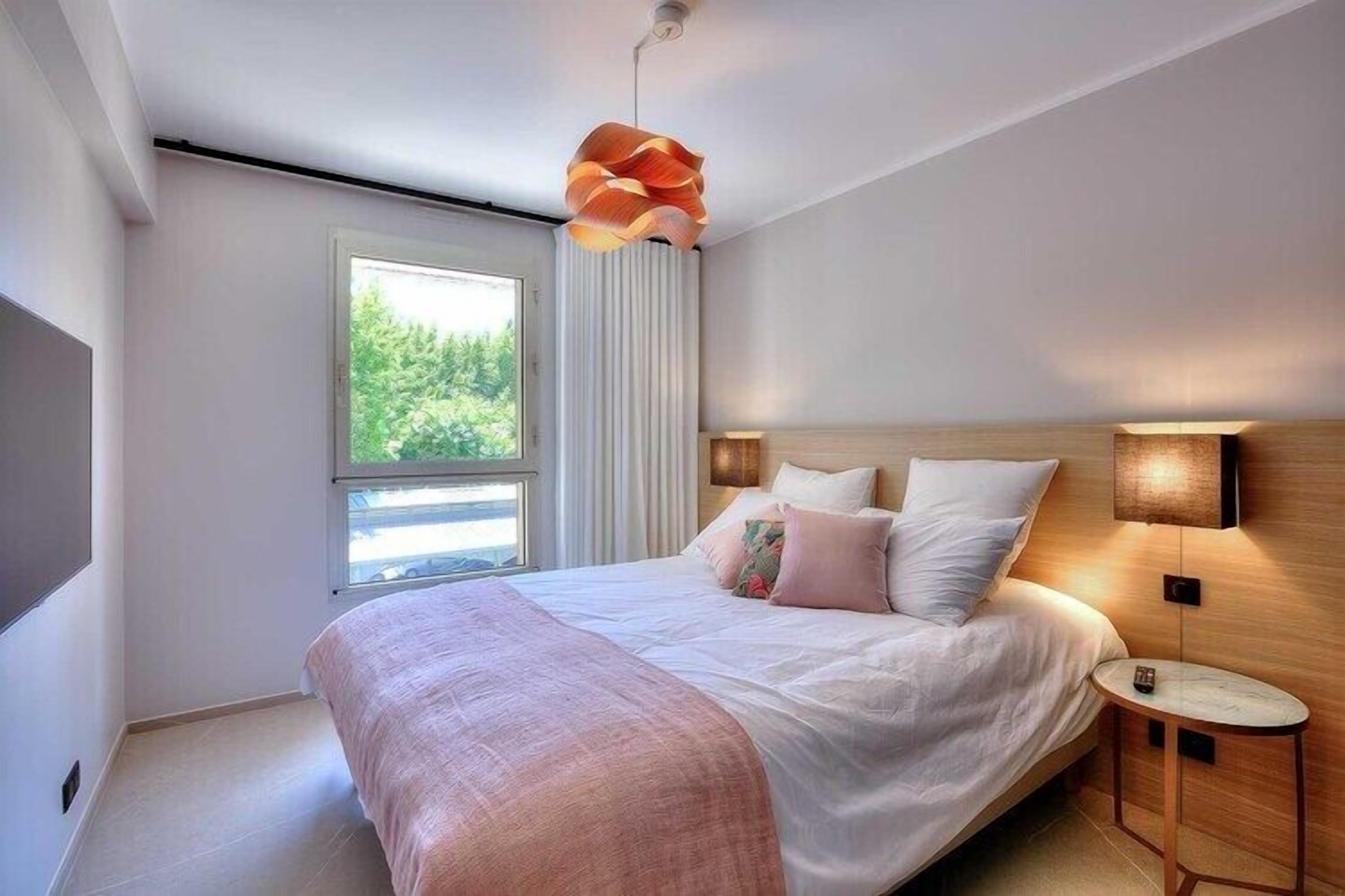 Camera da letto moderna con un letto grande, un comodino, una lampada a parete e una finestra con tende.