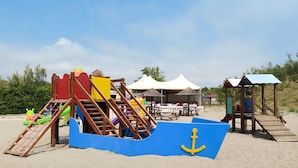 A beach play area with a slide, climbing structure, and a blue boat-shaped play mat with an anchor. - Rosolina Mare Club by Interhome (Rosolina Mare)