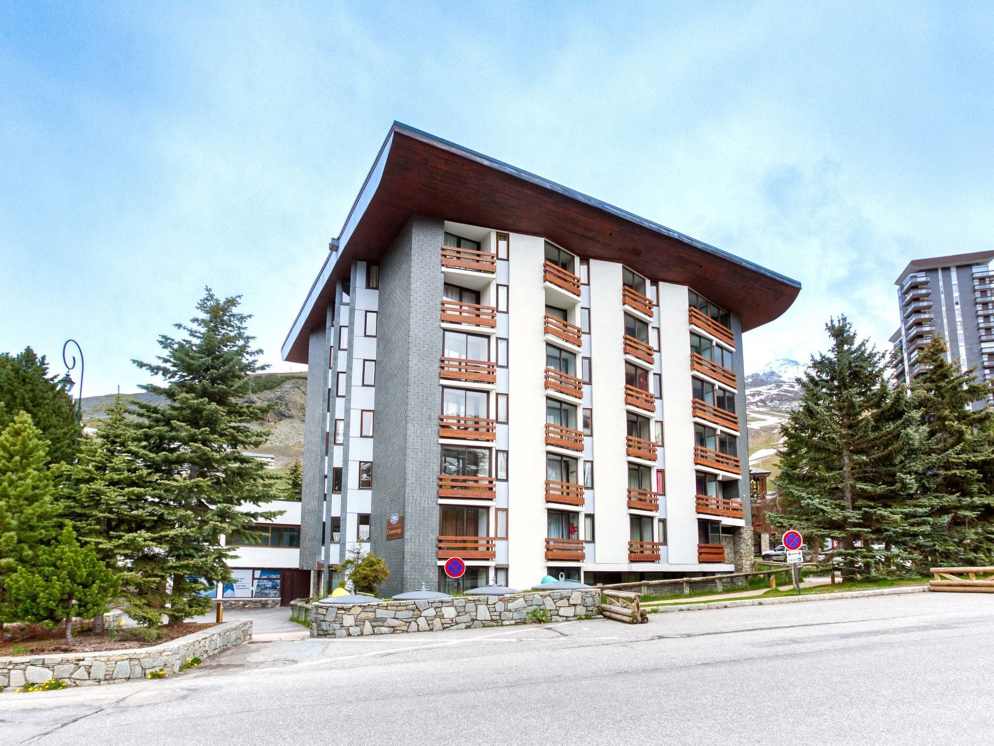 Ein mehrgeschossiges Hotel im modernen Stil, mit Balkonen mit Holzgeländern, einer Steinfassade und Blick auf eine Berglandschaft.