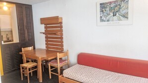 Ett litet rum med ett matbord och stolar i trä, en röd soffa och ett inramat konstverk på väggen.