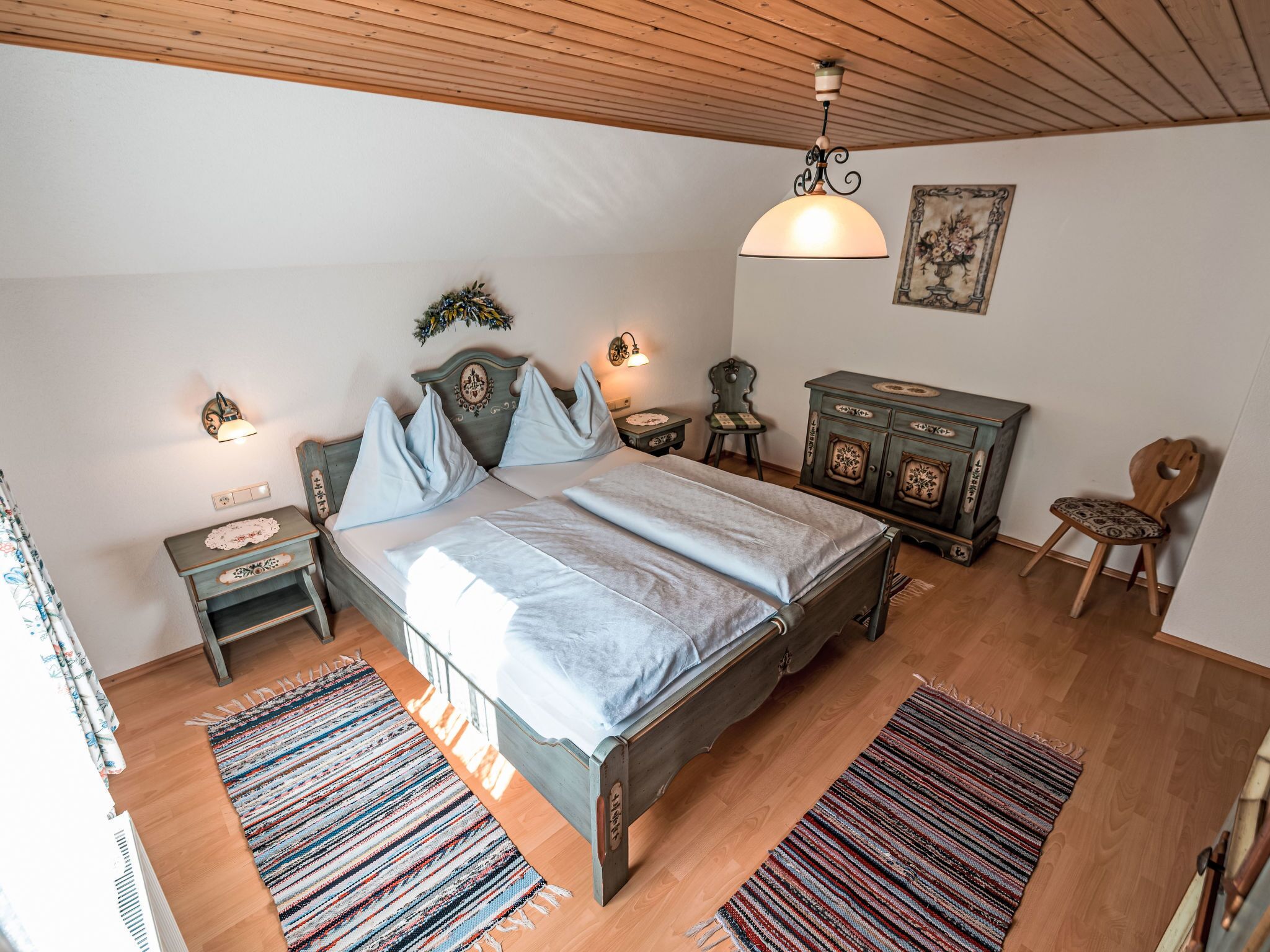 A bedroom with a wooden bed, a nightstand, a dresser, a chair, and a hanging light fixture.