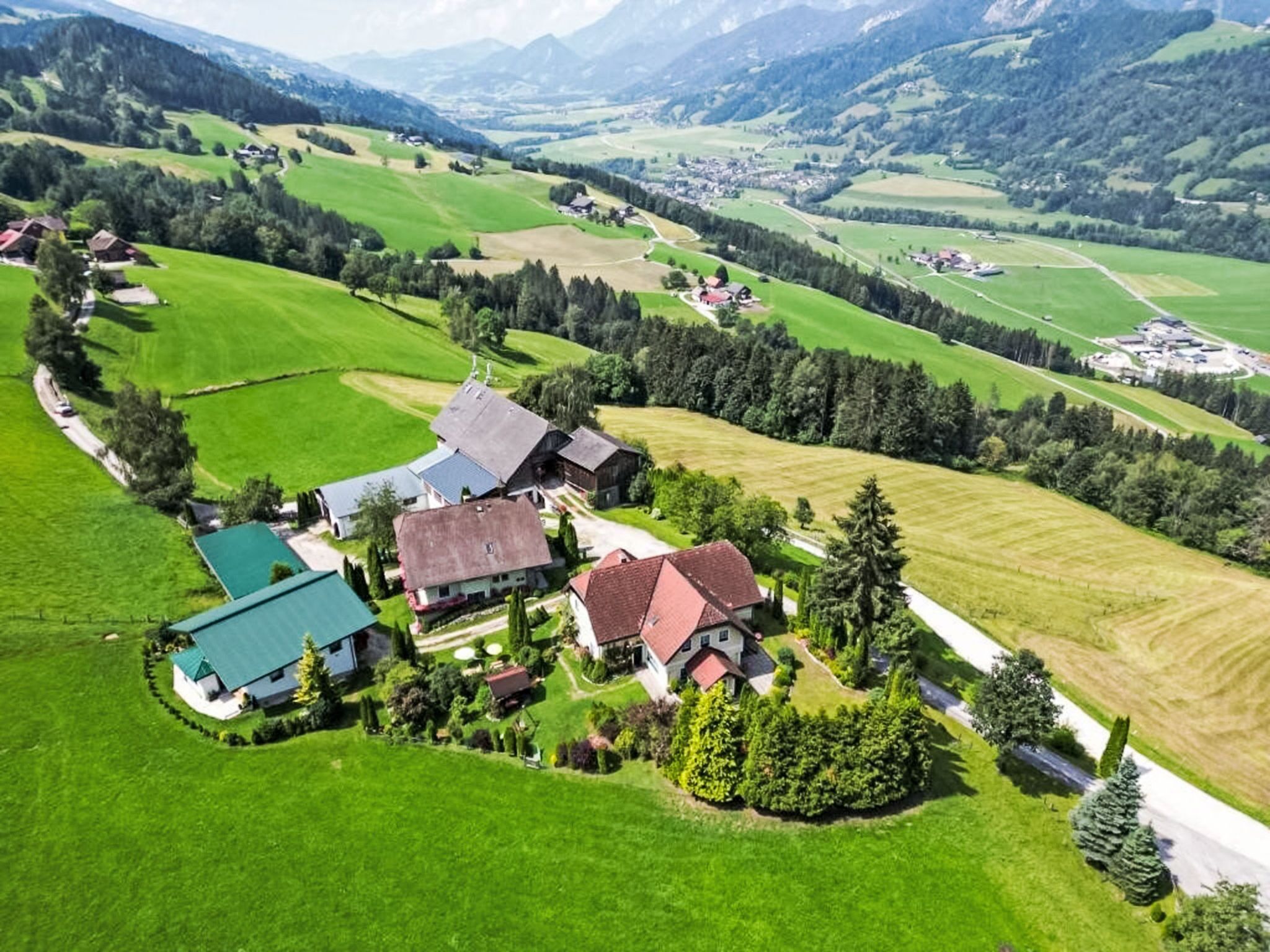 A rural landscape with a cluster of houses surrounded by green fields and mountains in the background.