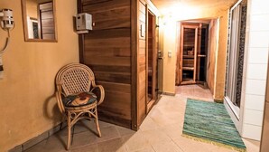 Un pasillo con una silla de mimbre, una puerta de madera y piso de baldosas.