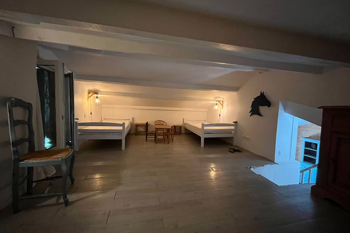 A room with two single beds, a wooden chair, a small table, and a wall-mounted light fixture.