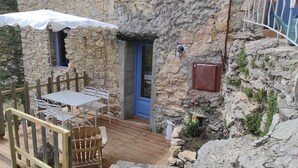 A rustic stone building with a wooden deck, a blue door, and a table with chairs. - Domaine du Cruvelet (Trigance)