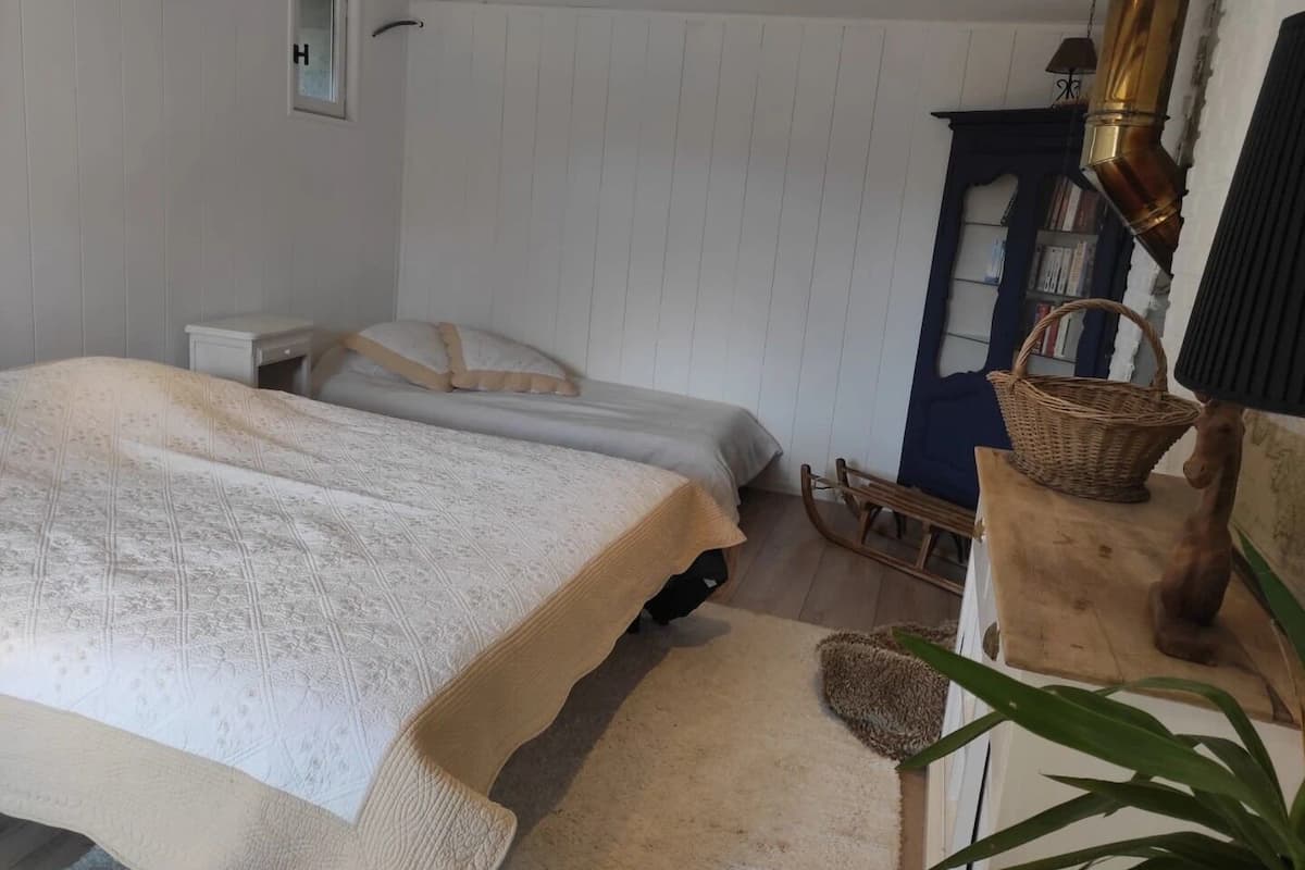 A bedroom with two beds, a small bedside table, a wooden rocking chair, a basket, and a lamp.